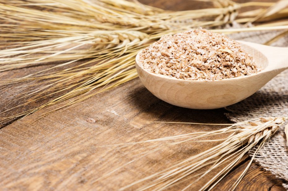 Close-up of wheat bran in wooden spoon with wheat ears. Dietary supplement to improve digestion. Source of dietary fiber. Wooden planks background. Side view, shallow depth of field